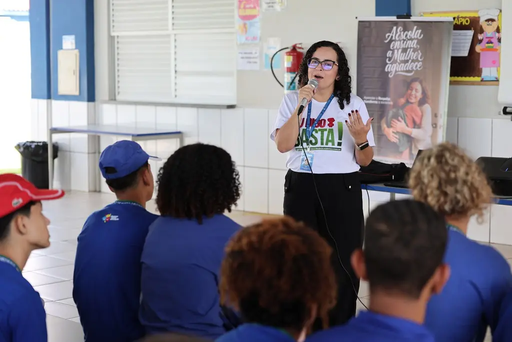 Foto horizontal em plano aberto que mostra a assessora da CEmulher, Adriany Carvalho, palestrando para diversos estudantes.