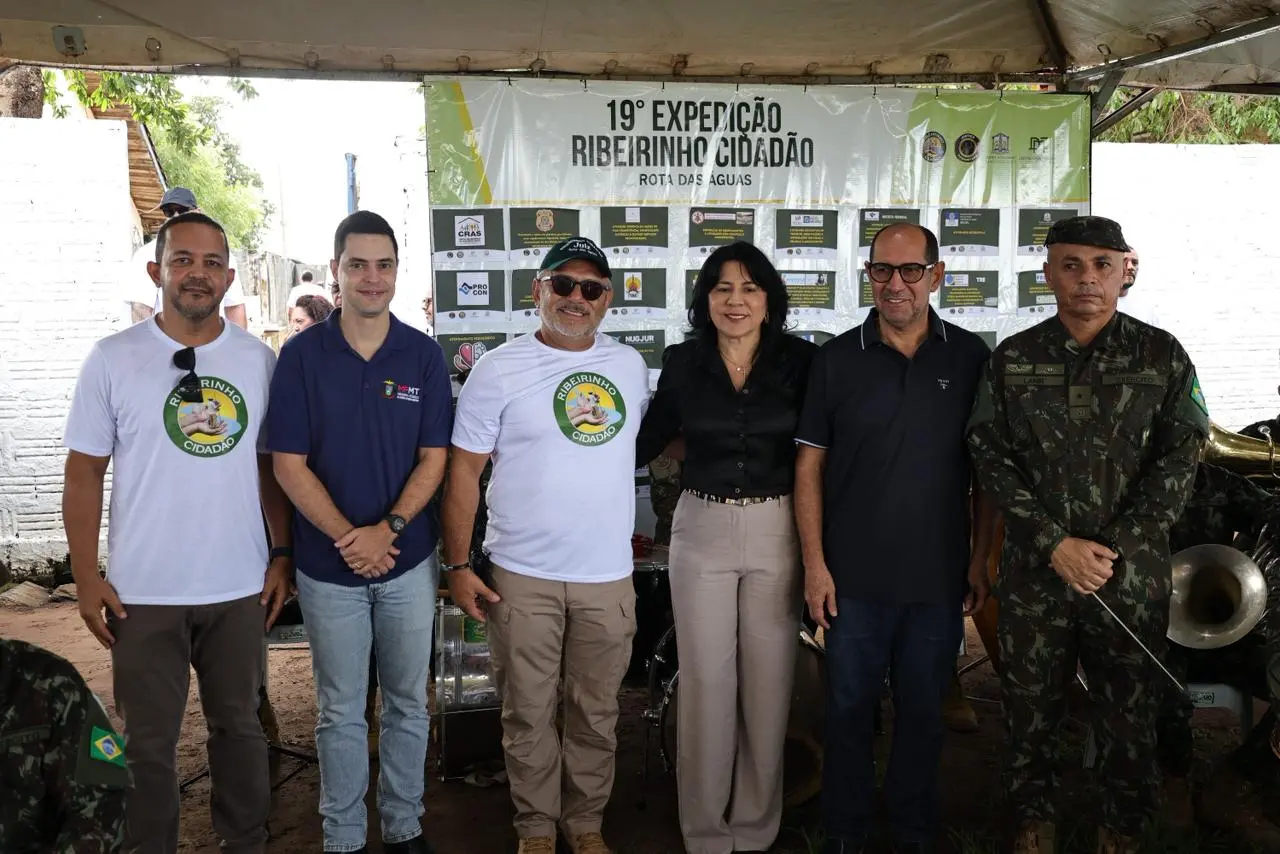 Grupo de seis pessoas posa à frente de um banner da 