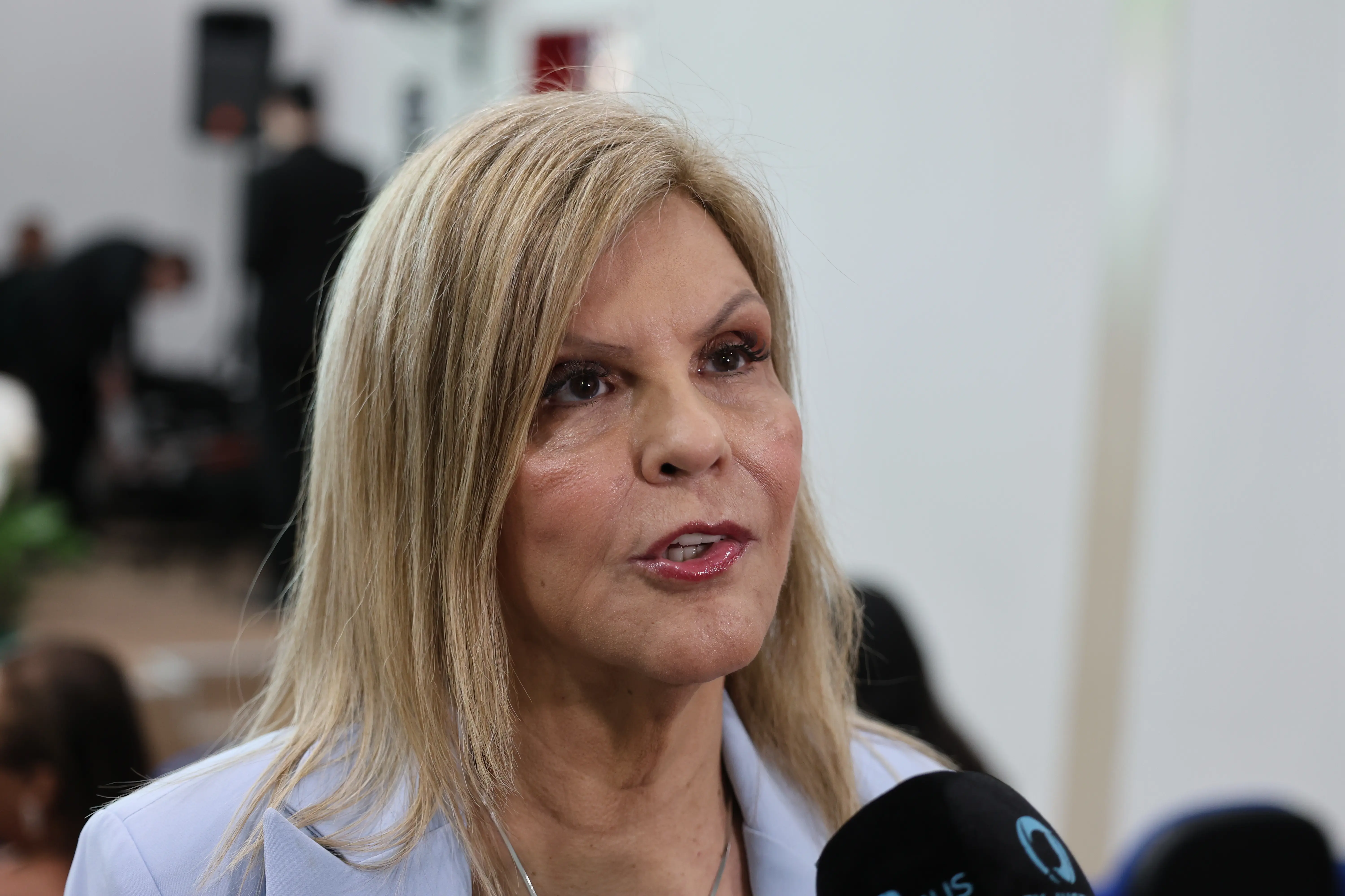 Desembargadora Nilza Pôssas de Carvalho é uma mulher loira, veste blazer azul-claro e está concedendo uma entrevista para a TV institucional.