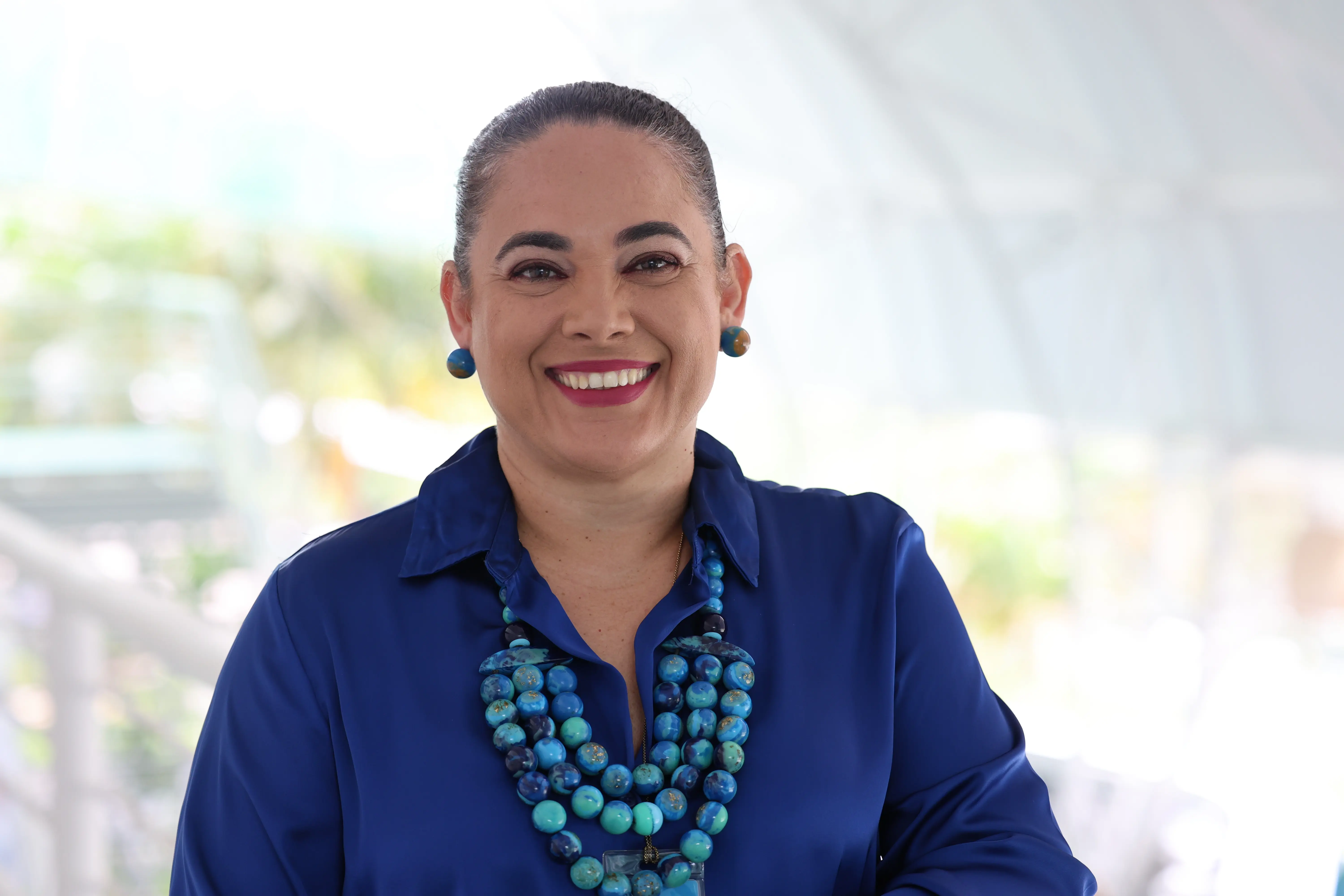 Retrato frontal da gestora Mariely Carvalho Steinmetz. Ela está sorridente, tem cabelos presos, veste camisa azul-escura e um colar de contas grandes em tons de azul e verde, com brincos combinando.