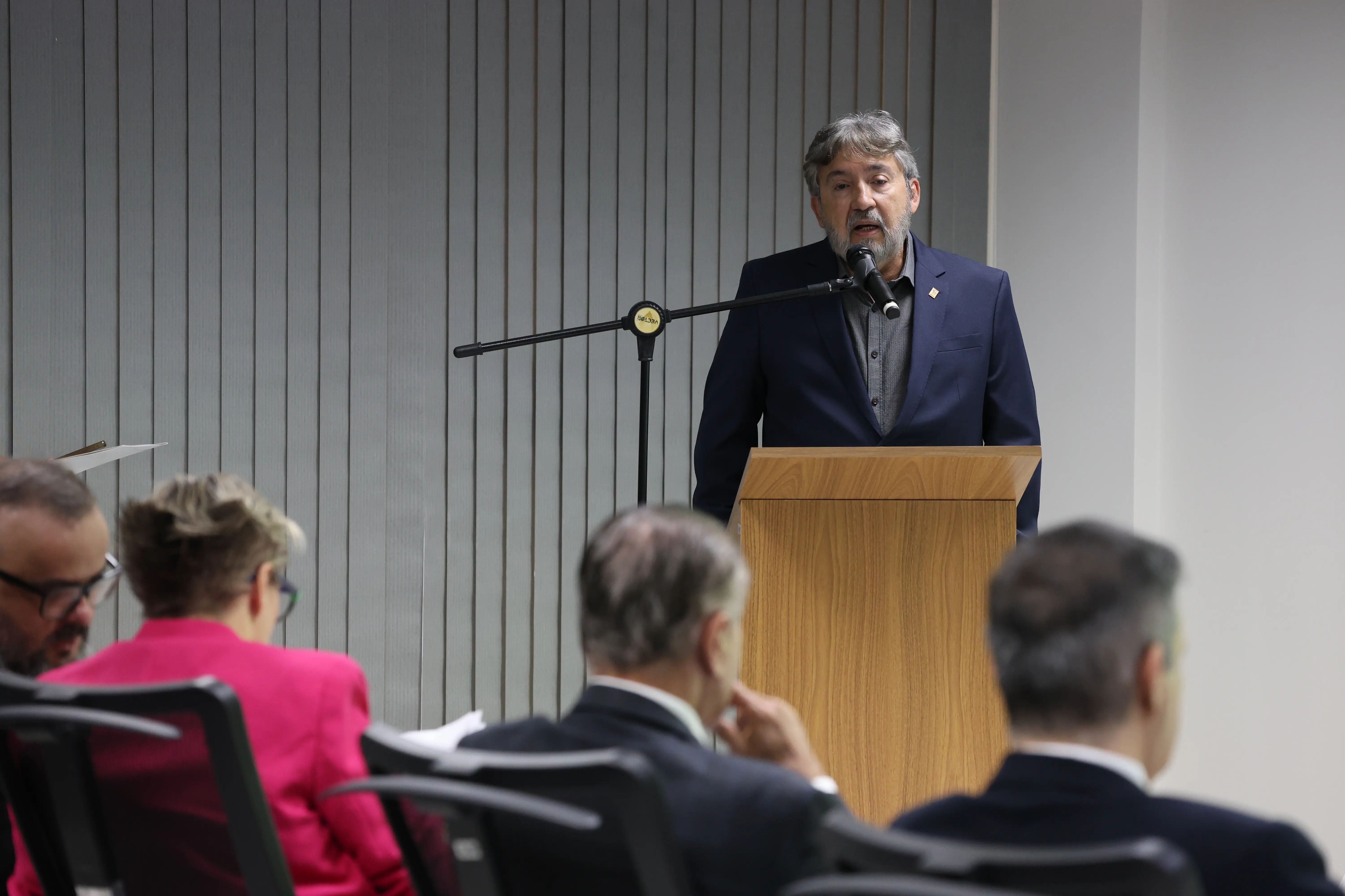 O desembargador Márcio Vidal, um homem de pele clara e barba grisalha vestindo paletó azul, fala ao microfone em um púlpito de madeira durante a abertura do evento. 