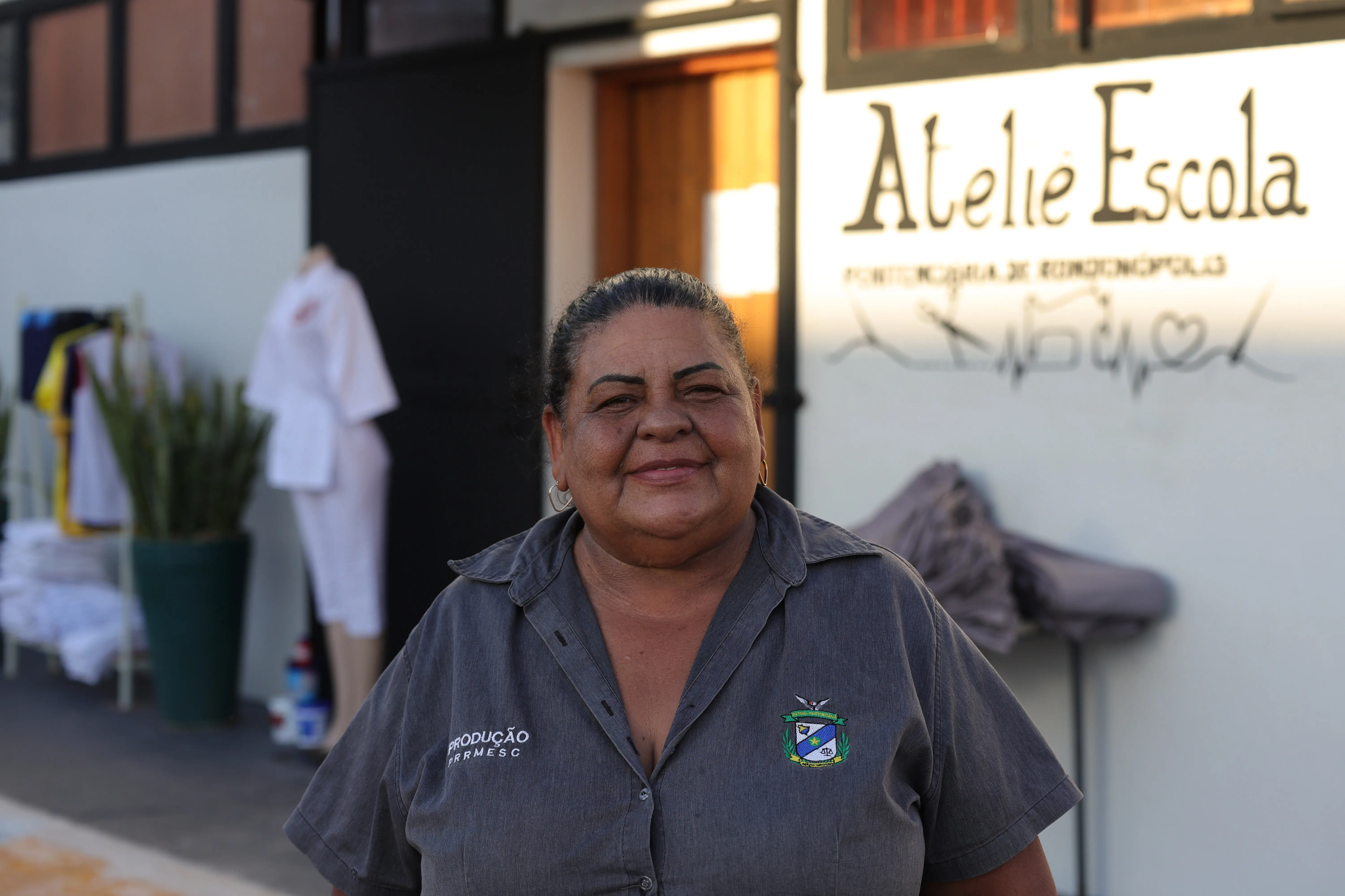 Retrato de uma mulher de cabelos presos, sorrindo em frente a uma parede branca com a inscrição 