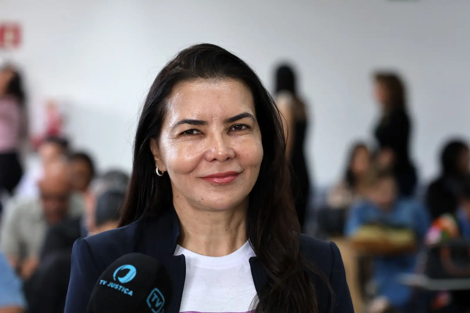 A imagem mostra a juíza auxiliar da Corregedoria, Anna Paula Gomes de Freitas, durante entrevista. Ela veste blazer escuro sobre camiseta da campanha Entrega Legal e aparece diante de microfones da imprensa.
