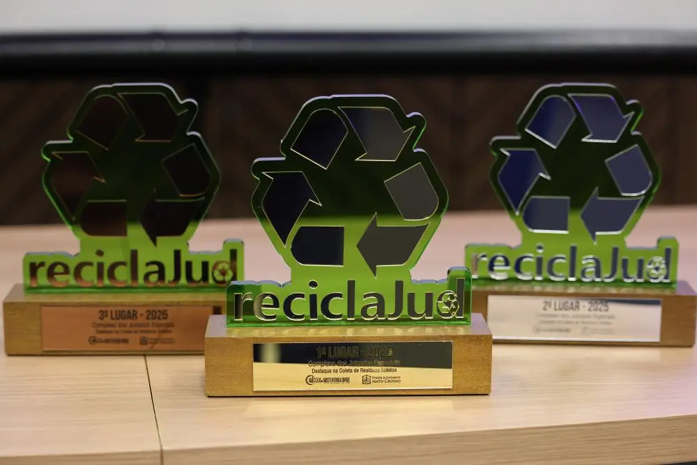 Foto colorida, na horizontal, que mostra uma mesa com vários troféus do Reciclajud. Os troféus são verdes e têm o símbolo da reciclagem e a palavra ReciclaJud.