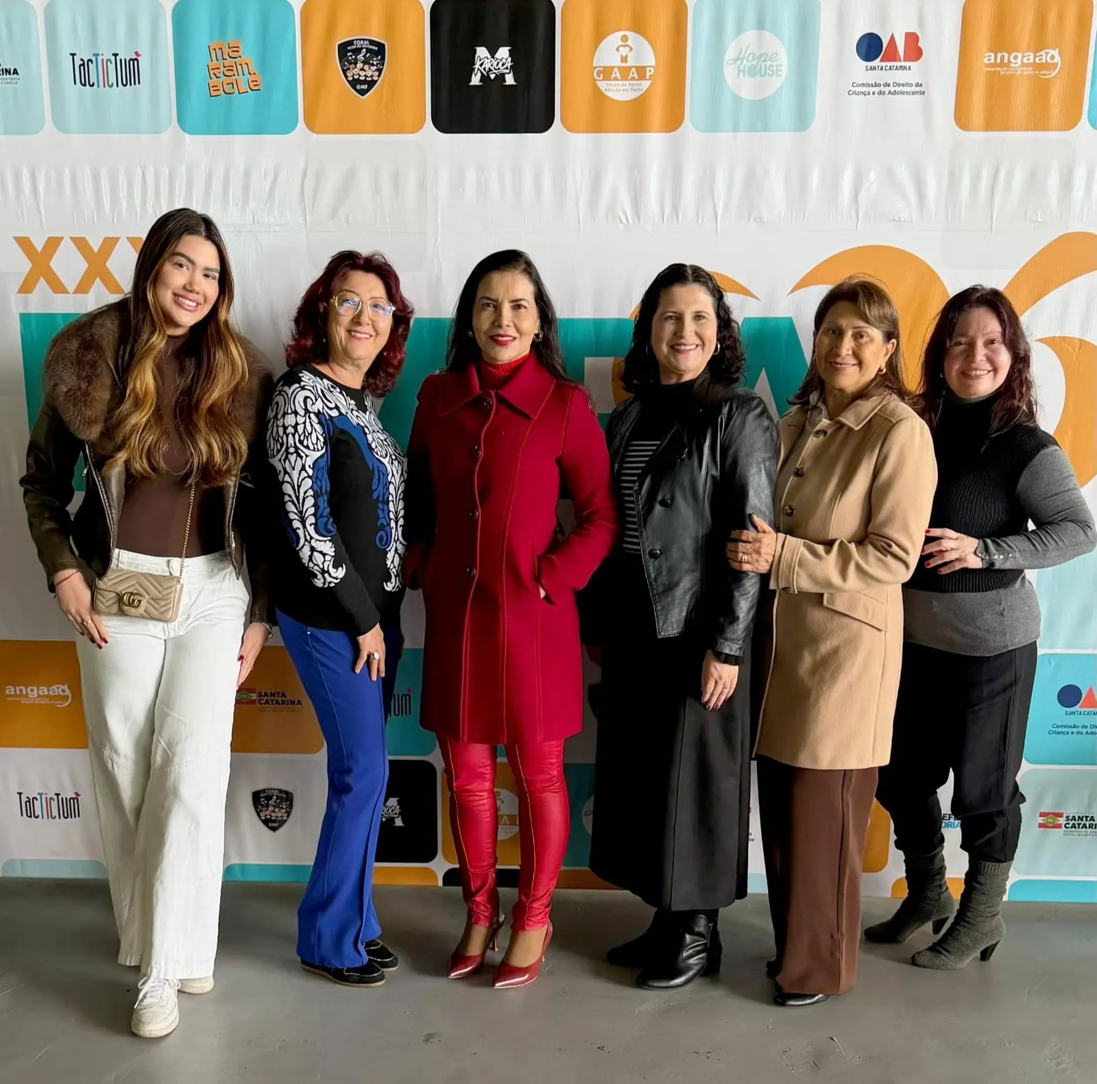 Seis mulheres posam lado a lado em frente ao painel oficial do ENAPA 2026, em Florianópolis (SC). O grupo representa a CEJA-MT e participa das atividades do encontro nacional sobre adoção e proteção integral.